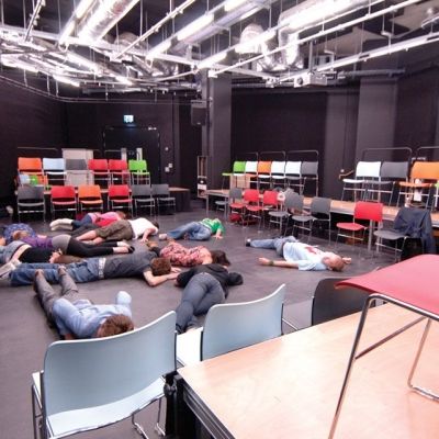 Students laying down on the floor in the drama hall in a performance